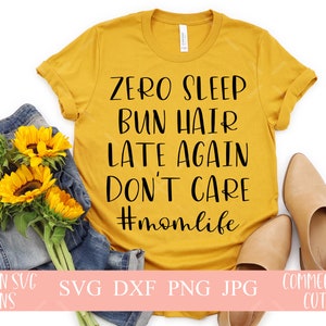 May include: A yellow t-shirt with the text "ZERO SLEEP BUN HAIR LATE AGAIN DON'T CARE #momlife" printed in black. The shirt is laying on a white surface with a pair of brown sandals and a pair of blue jeans with sunflowers.