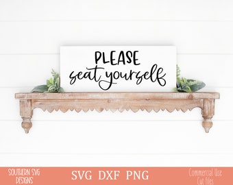 May include: A white rectangular sign with the words "PLEASE seat yourself" in black script. The sign is mounted on a decorative, light brown wooden shelf with a scalloped edge. Greenery accents the sign.