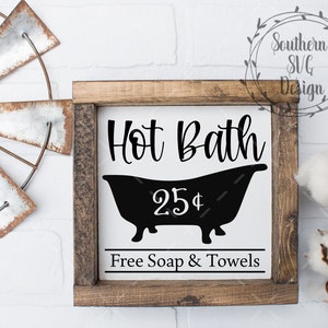 May include: A wooden sign with the text "Hot Bath 25$ Free Soap & Towels" in black lettering. The sign features a black silhouette of a bathtub.