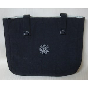 May include: A navy blue tote bag with two short handles and two smaller straps. The bag features a white embroidered logo on the front and white stitching along the top edge. The interior lining is a light blue and white pattern.