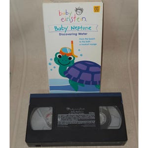 May include: A Baby Einstein "Baby Neptune: Discovering Water" VHS tape and box. The box features a cartoon turtle wearing a snorkel and the text "From the beach to the bath - a musical voyage."
