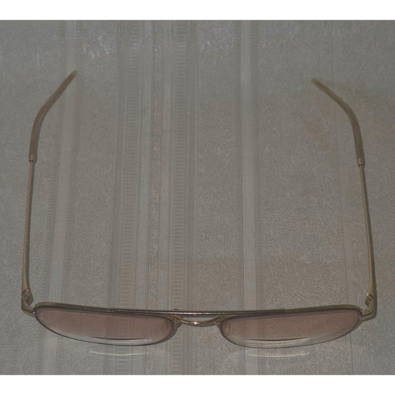 Puede incluir: Gafas de sol de aviador doradas con lentes tintadas en marr&oacute;n. Las gafas tienen un doble puente y varillas delgadas. Las lentes son de forma ovalada y la montura es de color dorado brillante. Las gafas se muestran sobre un fondo neutro.
