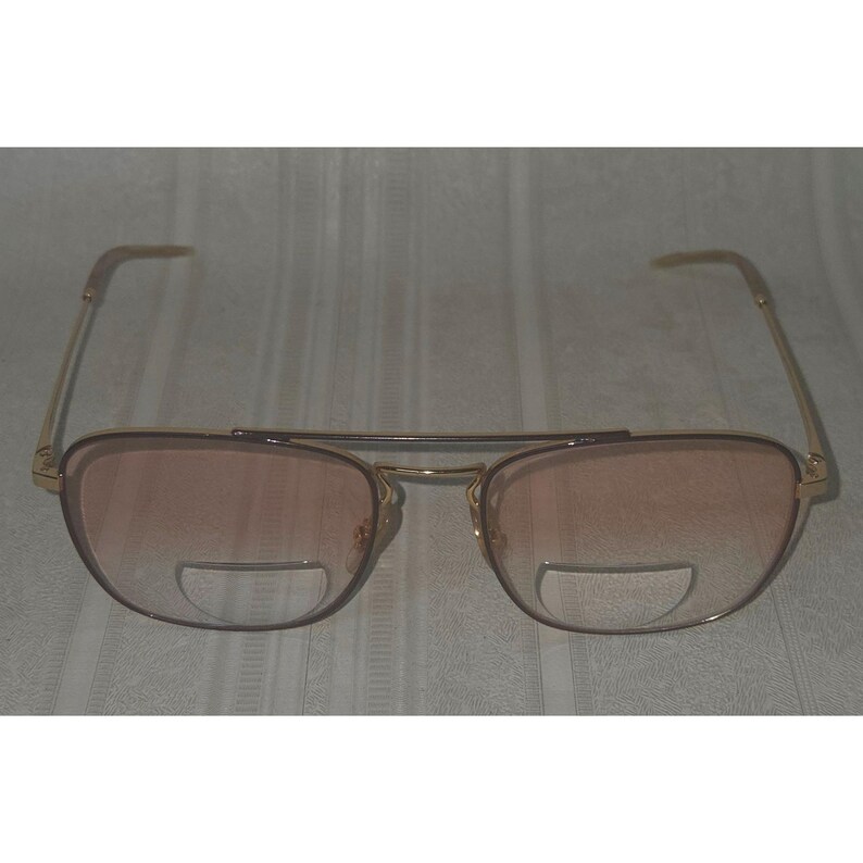 Puede incluir: Gafas con montura dorada, doble puente y lentes rosas degradadas. La parte inferior de cada lente tiene una inserci&oacute;n clara y circular. Las patillas son finas y doradas, curv&aacute;ndose suavemente. Dise&ntilde;o de inspiraci&oacute;n vintage.