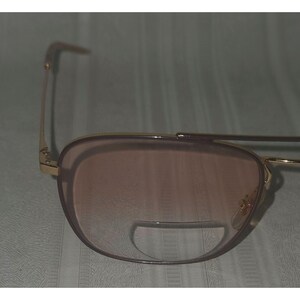 Puede incluir: Gafas de sol con montura dorada y lentes tintadas en marr&oacute;n. Las gafas tienen una forma de aviador cl&aacute;sica con doble puente y barra superior curvada. Las lentes tienen un color degradado, que pasa de un tono m&aacute;s oscuro en la parte superior a uno m&aacute;s claro en la inferior.