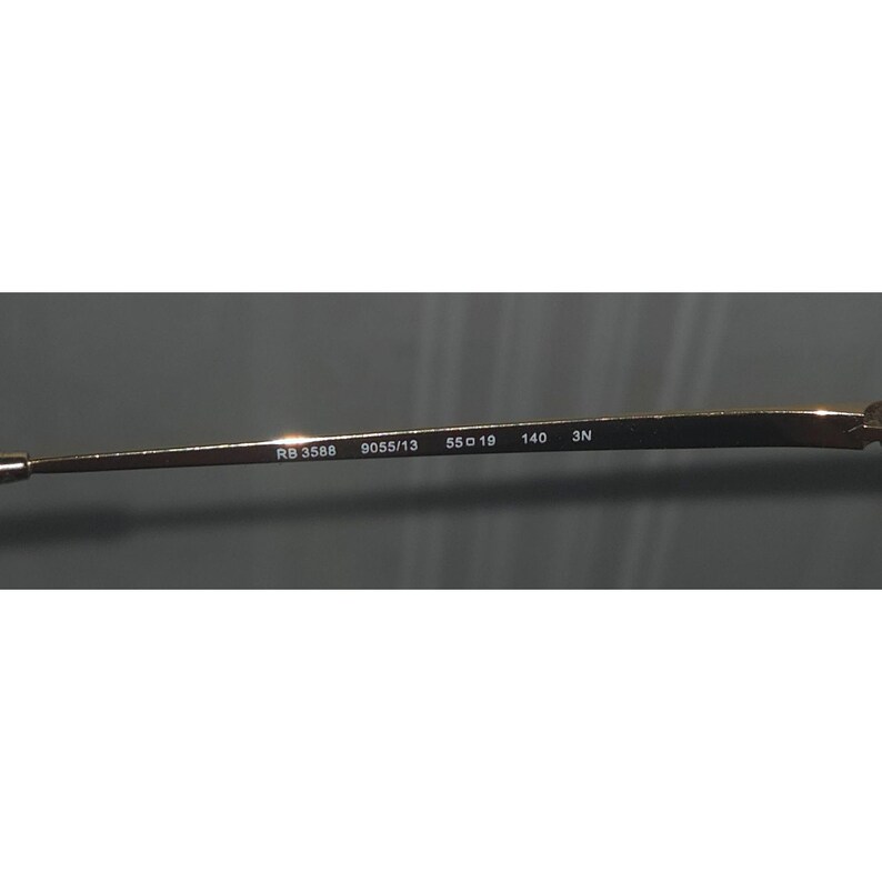 Puede incluir: Primer plano de la patilla de unas gafas. La patilla es de color dorado y tiene el texto "RB 3588 9055/13 55o19 140 3N" impreso.