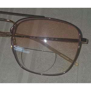 Puede incluir: Gafas de sol con montura dorada y lentes degradadas. Las lentes hacen una transici&oacute;n de un melocot&oacute;n claro a un tono m&aacute;s oscuro. La montura tiene forma rectangular con un dise&ntilde;o de doble puente. Las patillas son finas y doradas, con texto impreso en la montura.