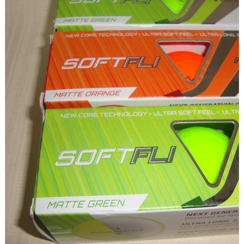 May include: Two boxes of Softfli golf balls. The top box is orange with the text "Matte Orange" and the bottom box is green with the text "Matte Green". Both boxes feature the Softfli logo and the text "New Core Technology Ultra Soft Feel Ultra Long".