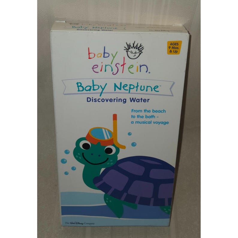 May include: A white box with the "Baby Einstein" logo and "Baby Neptune Discovering Water." The box features a cartoon turtle wearing a snorkel. Text on the box reads "From the beach to the bath - a musical voyage" and "AGES 9 Mos. & Up."