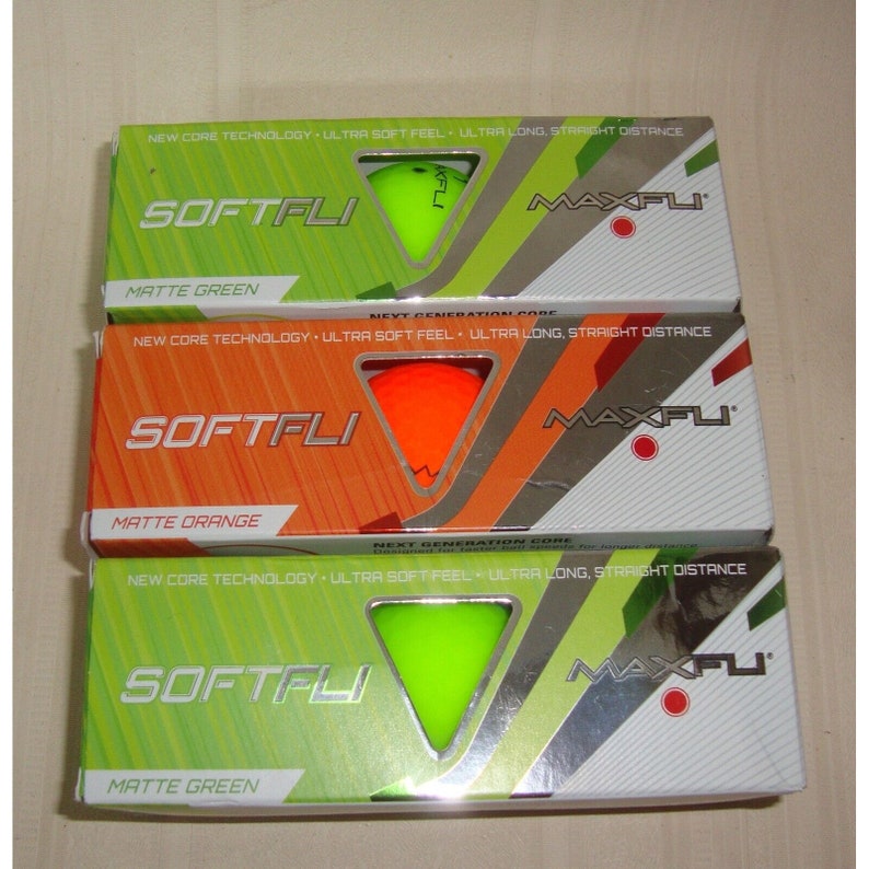 May include: Three boxes of golf balls, each with a different color ball on the front. The boxes are green, orange, and green. The boxes have the words "SOFTFLI" and "MAXFLI" on them. The text on the boxes reads "NEW CORE TECHNOLOGY ULTRA SOFT FEEL ULTRA LONG, STRAIGHT DISTANCE".
