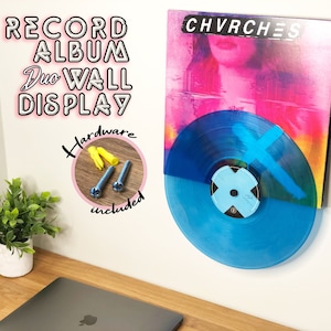 Peut inclure: Un disque vinyle bleu avec une étiquette bleu et blanc est monté sur un mur blanc. Le disque fait partie d'un présentoir mural pour deux albums vinyles. La pochette de l'album est visible derrière le disque et présente le groupe CHVRCHES. Le texte "RECORD ALBUM DUO WALL DISPLAY" est écrit en lettres roses sur le mur. Le texte "Hardware included" est écrit dans un cercle rose sur le mur.