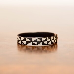 May include: A black and white geometric patterned bracelet with a copper clasp.