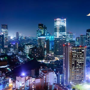 May include: A nighttime cityscape with numerous illuminated skyscrapers and buildings. The image is dominated by the dark blue sky, with a crescent moon in the upper right corner. The city lights create a vibrant, colorful display.