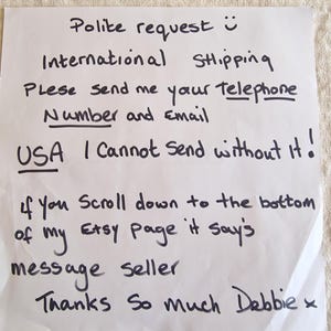 May include: A handwritten note on white paper with black ink. The text requests a phone number and email for international shipping, and mentions Etsy. The note is signed "Debbie".