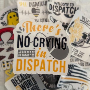 May include: A collection of stickers with various designs and text related to dispatchers. The central sticker reads "There's No Crying in Dispatch" in orange and black. Other stickers feature phrases like "911 Dispatcher" and "Welcome to Dispatch".