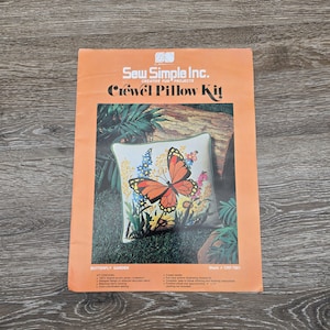 May include: An orange and white "Sew Simple Inc. Crewel Pillow Kit" box. The kit features a pillow design with a butterfly and flowers. The pillow is approximately 14 x 14 inches.