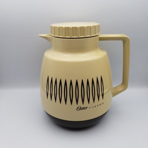 May include: A beige Oster Thermo carafe with a black lid and a black and white geometric design. The carafe has a black base and the text "Oster Thermo" is printed on the side.