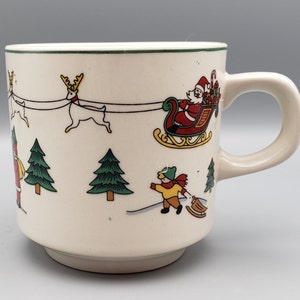 May include: White ceramic Christmas mug with a green rim. The mug features a festive scene with Santa Claus in a red sleigh pulled by reindeer, children playing in the snow, and Christmas trees.