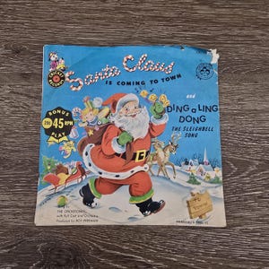 May include: Vintage 45 RPM record featuring Santa Claus on the cover, dressed in a red suit and carrying a sack. The record is titled "Santa Claus is Coming to Town" and "Ding a Ling Dong". The cover has a blue background.