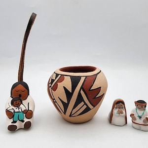 May include: A collection of Native American pottery and figurines. The set includes a small, round pot with geometric designs in black, red, and beige, along with several small figurines depicting people. A leather cord is attached to one figurine.