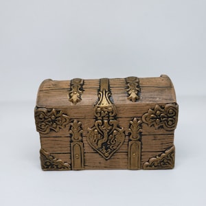 May include: A small wooden treasure chest with gold accents and ornate metal details. The chest has a hinged lid and a lock.