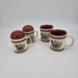 May include: Two ceramic mugs and two matching salt and pepper shakers featuring a cream-colored base with a dark red rim. Each piece is decorated with a repeating pattern of a hen and chicks, accented by a dark red and white polka dot border.