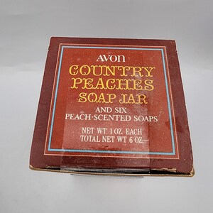 May include: A brown box with the text "AVON COUNTRY PEACHES SOAP JAR" in gold lettering. The box also states "AND SIX PEACH-SCENTED SOAPS" and "NET WT 1 OZ. EACH TOTAL NET WT 6 OZ."