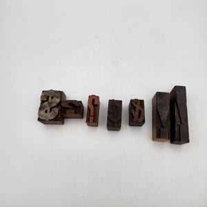May include: A collection of six vintage wooden letterpress blocks featuring various symbols and punctuation marks, including a dollar sign, an ampersand, a question mark, a cent sign, a small ampersand, and two vertical exclamation point marks.