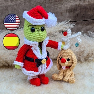 Puede incluir: Un Grinch verde de crochet que lleva un traje de Papá Noel rojo con ribete blanco y un gorro blanco con pompón. El Grinch sostiene un reno de crochet con la nariz roja y el pelo marrón.