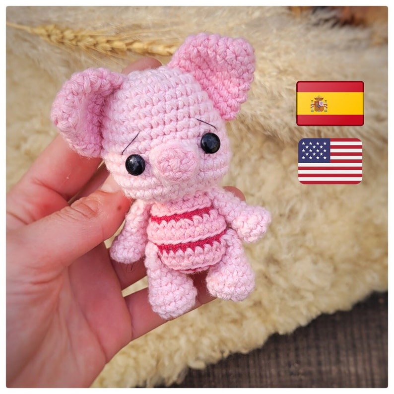 Puede incluir: Un juguete de cerdo de crochet rosa con ojos negros y un cuerpo a rayas rosa y blanco. El juguete est&aacute; siendo sostenido en una mano.