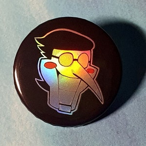 May include: A circular pin-back button featuring a holographic, stylized character head with a long nose, round glasses, and red cheek spots against a solid black background. The design reflects light with rainbow colors, and the text TheFunctionCreep is visible.