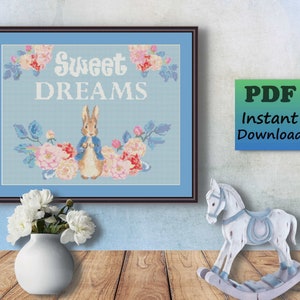 May include: Cross stitch pattern featuring a sweet dreams design with a bunny rabbit surrounded by flowers. The pattern is in a blue frame and has the text "Sweet Dreams" on it.