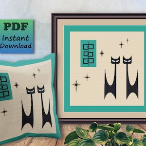 May include: A cross-stitch pattern featuring two black cats with blue eyes, a teal window, and white stars on a beige background. The pattern is framed in a black frame and is displayed on a wall with a green plant in the foreground.