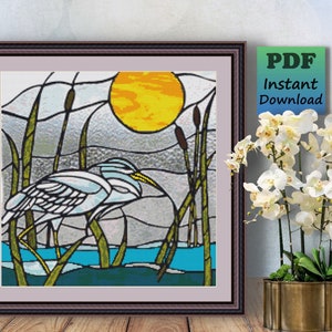 May include: A stained glass style cross stitch pattern featuring a white heron standing in a marsh with tall green reeds and a yellow sun in the background.