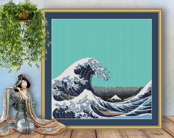 May include: A framed cross-stitch artwork depicting a blue and white wave crashing against a mountain in the background. The sky is a light turquoise colour.