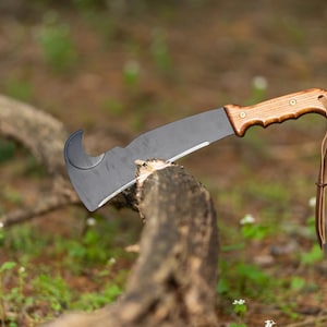 May include: A black and brown machete with a curved blade and a wooden handle. The machete is resting on a branch.