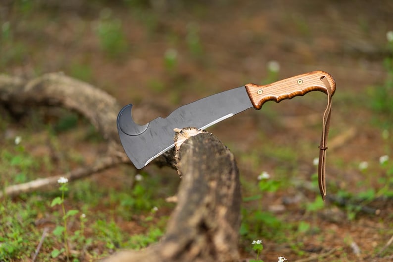 May include: A black and brown machete with a curved blade and a wooden handle. The machete is resting on a branch.