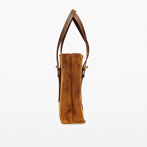 May include: A brown leather tote bag with two top handles and a brown leather strap. The bag has a flap closure with a gold buckle.