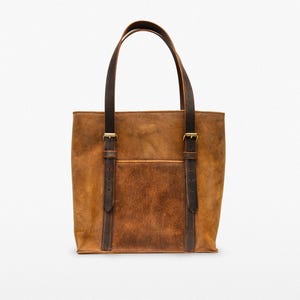 May include: A brown leather tote bag with dark brown leather straps and gold buckles. The bag has a front pocket.