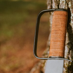 May include: A black metal handle with a brown leather wrap. The handle is attached to a blade, which is not visible in the image.