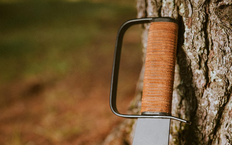 May include: A black metal handle with a brown leather wrap. The handle is attached to a blade, which is not visible in the image.