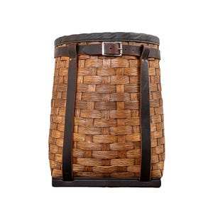 May include: A brown wicker basket with leather straps and a buckle. The basket has a black fabric lining and a black base.