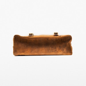 May include: A brown leather satchel bag with two buckles on the front. The bag is made of a distressed leather and has a worn look.