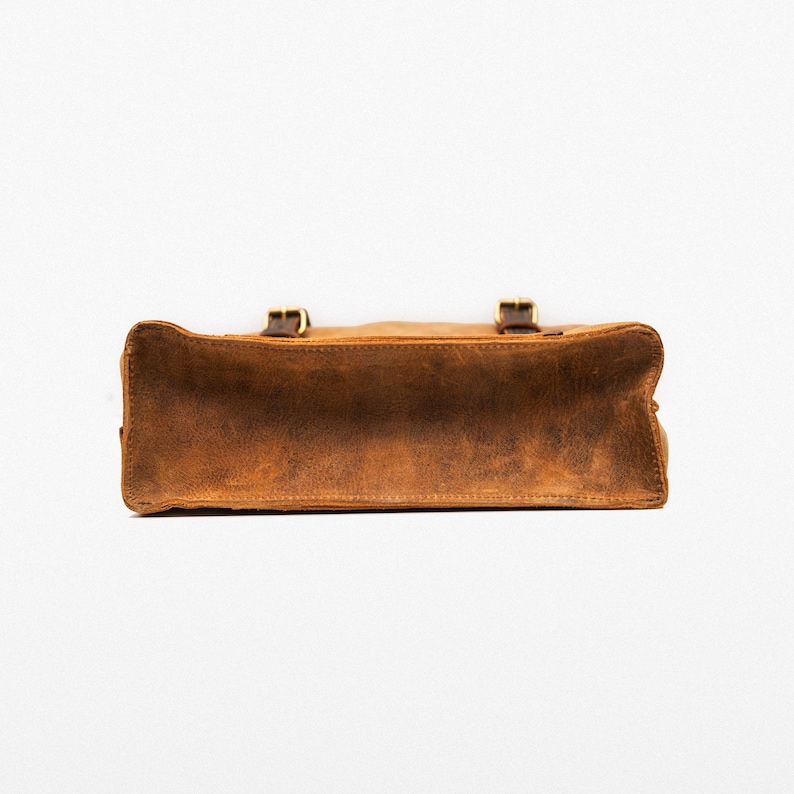 May include: A brown leather satchel bag with two buckles on the front. The bag is made of a distressed leather and has a worn look.