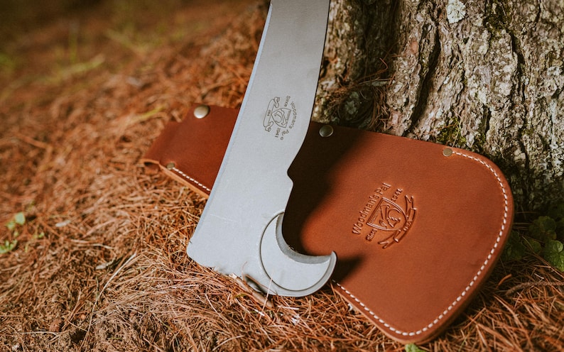 May include: A silver-colored tool with a curved blade and a leather sheath. The sheath is brown and has the text "Western Trail" embossed on it.