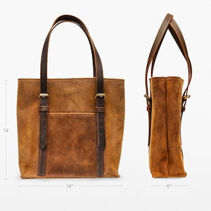 May include: A brown leather tote bag with two adjustable straps and a front pocket. The bag measures 14 inches wide and 14 inches tall.