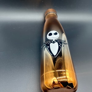 Op de afbeelding: Een gouden en zwarte roestvrijstalen waterfles met een zwart-witte afbeelding van Jack Skellington uit The Nightmare Before Christmas.