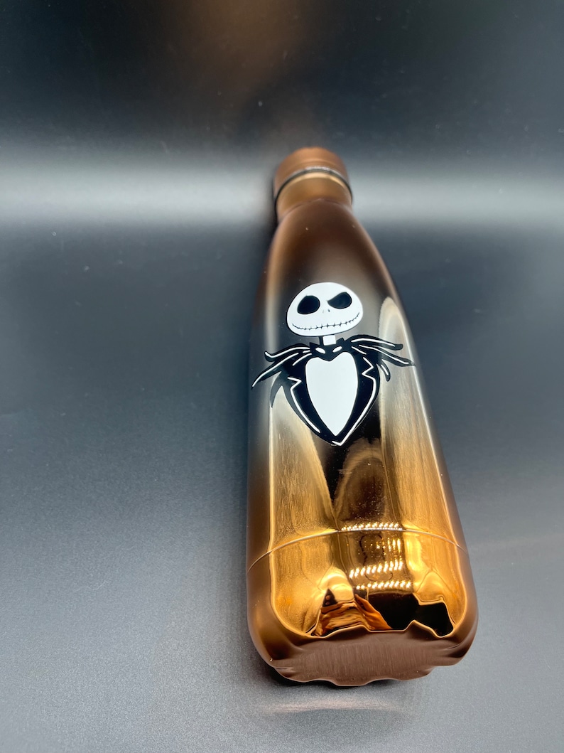 Op de afbeelding: Een gouden en zwarte roestvrijstalen waterfles met een zwart-witte afbeelding van Jack Skellington uit The Nightmare Before Christmas.
