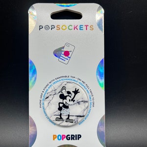May include: A PopSockets PopGrip featuring a marble design with a black and white Mickey Mouse graphic. The packaging is white with holographic accents and the PopSockets and PopGrip logos. The product is a phone grip and stand.