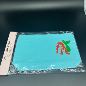 May include: A light blue fabric pouch with a red and green mermaid silhouette design.