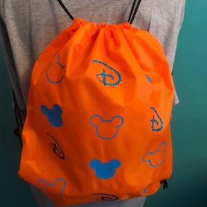 May include: Orange drawstring bag with blue Mickey Mouse heads and Disney logos. The bag is made of a lightweight fabric and has a drawstring closure.